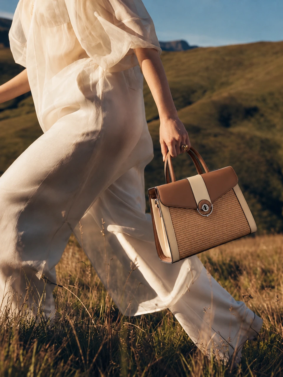 SU QUEENA brown and ivory woven-panel top-handle bag with a flowing ivory outfit in sunlit hills.