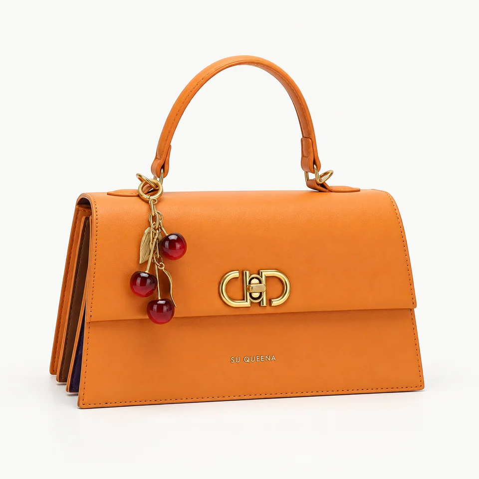 SU QUEENA 3244 orange bag with gold closure and cherry charm, isolated on off-white.